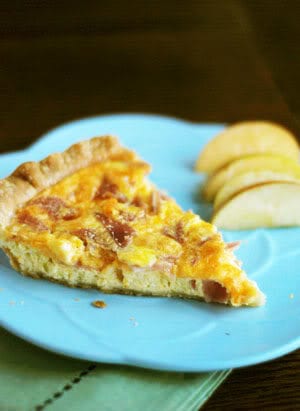 a slice of egg quiche on a blue plate with apple slices beside it