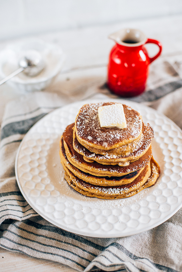 white plate with tan cloth and a stack of 5 pumpkin pancakes with butter