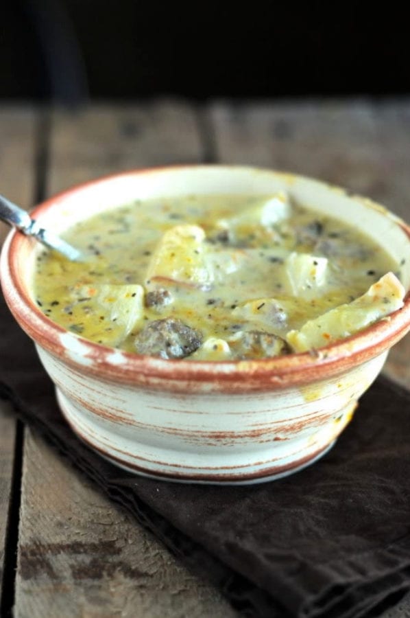 A bowl of potatoes and ground beef in a cheesy broth with a rustic wood background