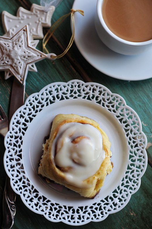 A homemade cinnamon roll on a white plate with Christmas ornaments and tea