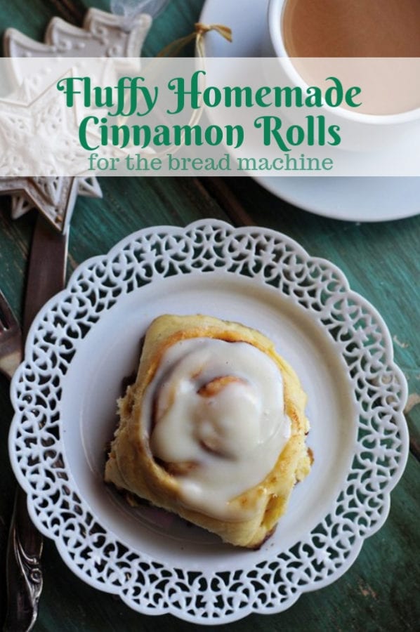 A large cinnamon roll on a white plate with green table, tea and ornaments