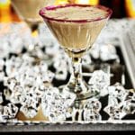 A martini glass with red glitter on the rim filled with a chocolate martini. Glass cubes on a platter.