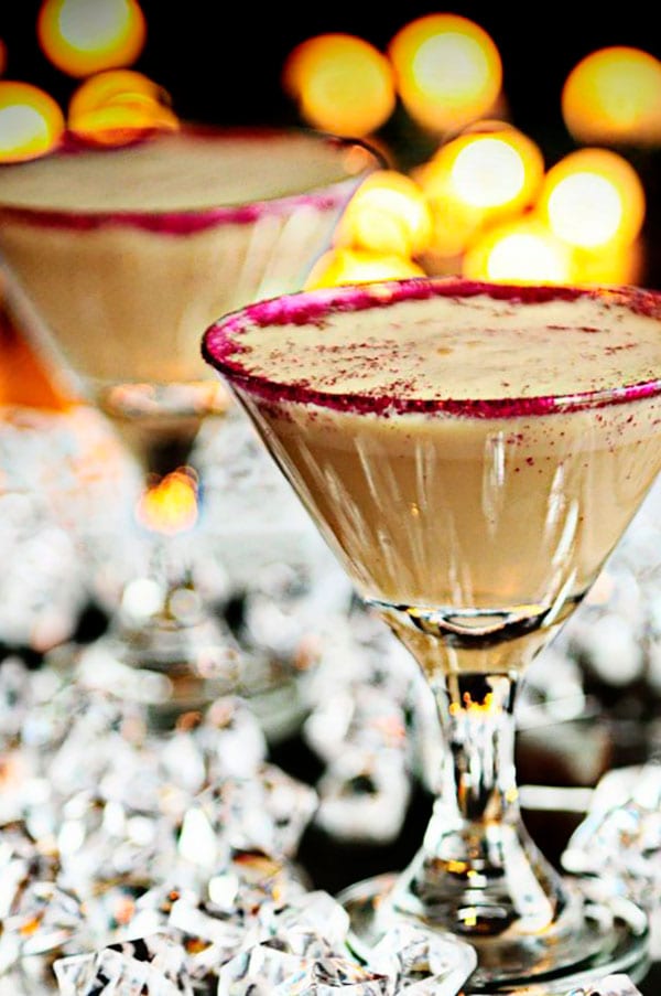 A chocolate cocktail in a small martini glass with the glow of white lights in the background