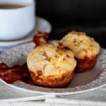 Image is of bacon and cheese breakfast muffins on a white plate with a cup of coffee