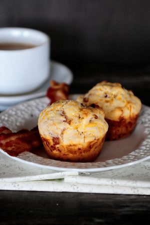 Image is of bacon and cheese breakfast muffins on a white plate with a cup of coffee