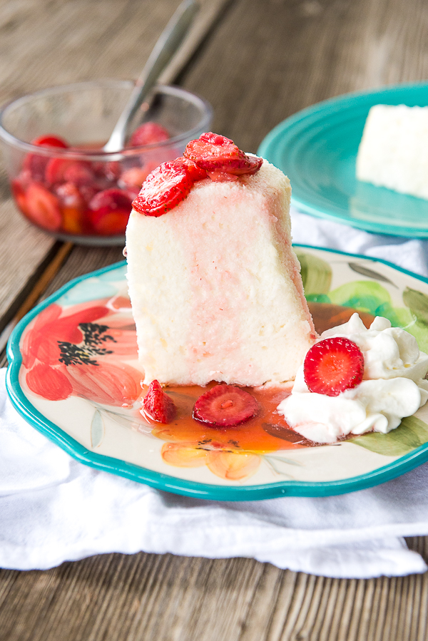 Image is two slices of homemade angel food cake on a floral plate topped with strawberries