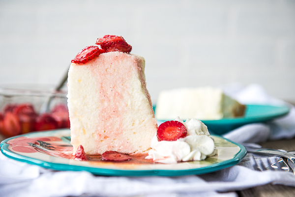 Image is horizontal and is of a slice of angel food cake with strawberries on top and whipped cream on the side