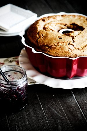 Image shows a bundt cake in a pan on a white plate and dark background