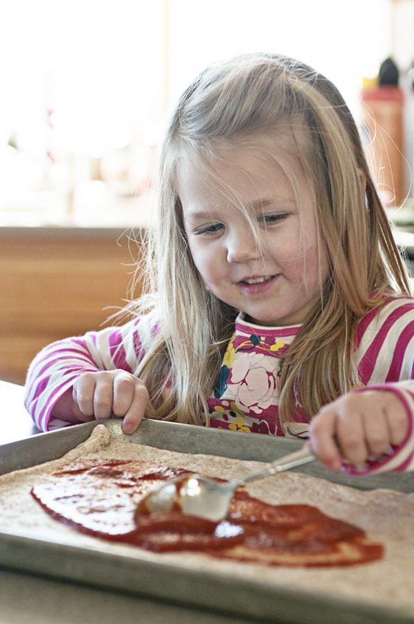 Little Girl Spreading Pizza Sauce on Pizza Dough