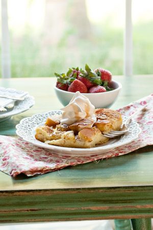French Toast Casserole on a white plate with a colorful napkin. There's a bowl of strawberries in the background.