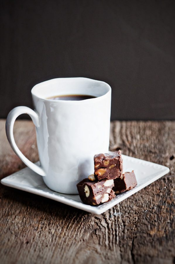 Coffee cup on a white plate with three pieces of chocolate cashew fudge