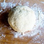 A ball of pizza dough on a wooden cutting board
