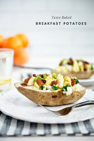 Twice Baked Breakfast Potatoes with eggs, bacon and spinach served on a white plate with white brick background