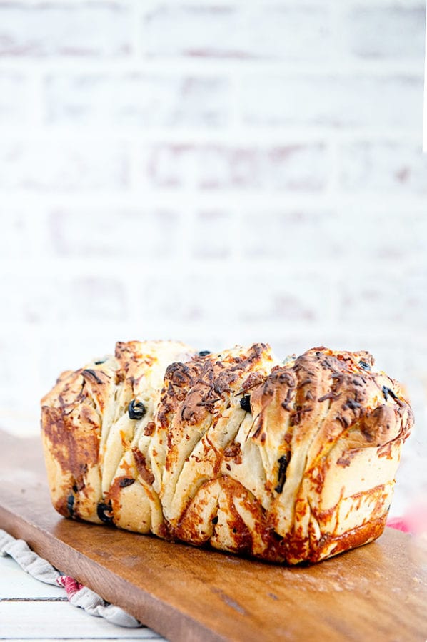 A savory loaf of pull apart bread on a wood cutting board with a white brick background