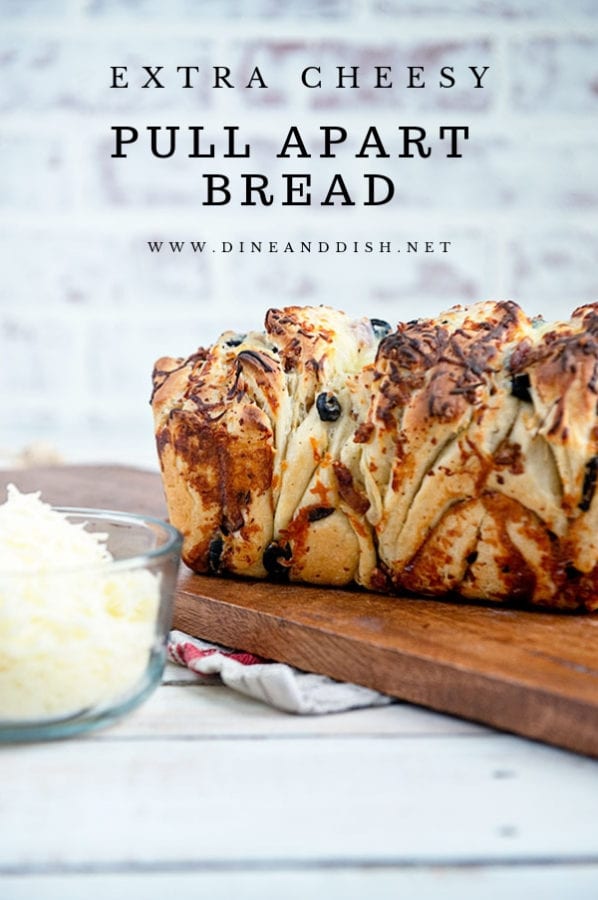 A loaf of cheese pull apart bread on a wooden board with a white brick background.