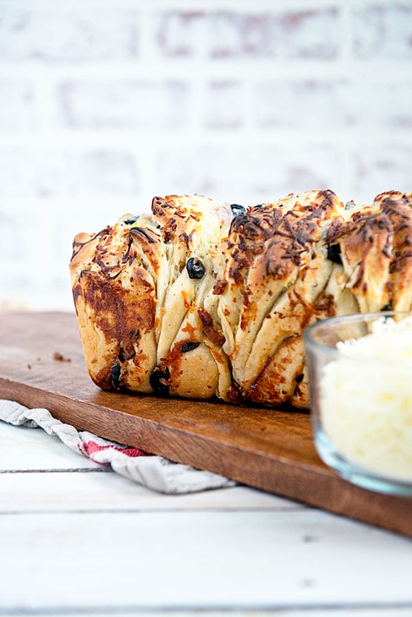 A savory loaf of pull apart bread on a wooden cutting board with white brick background