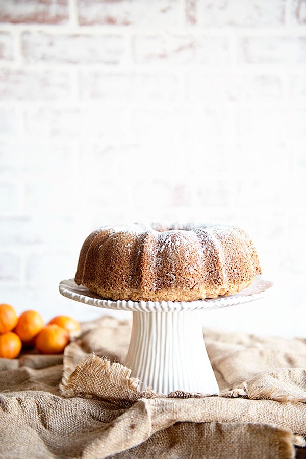 Bright white brick background with oranges and a bundt cake on a white cake stand