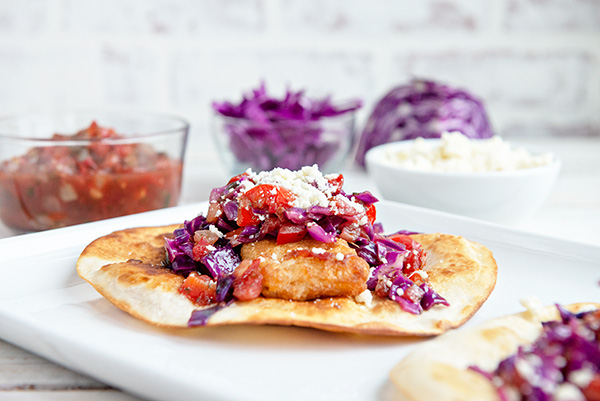 horizontal image of beer battered fish tostadas with purple cabbage on a white background