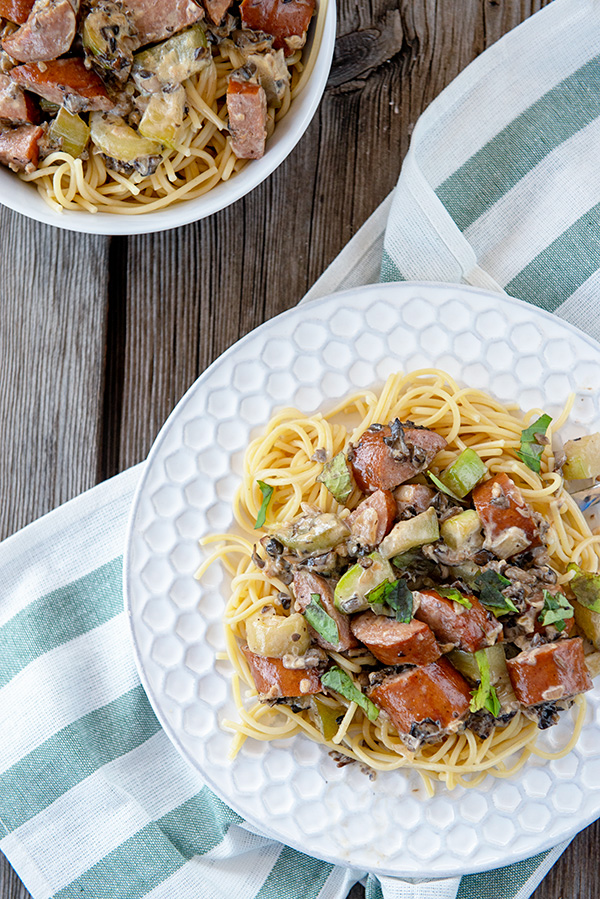 White plate with with creamy chopped mushroom sauce over pasta and kielbasa sausage.