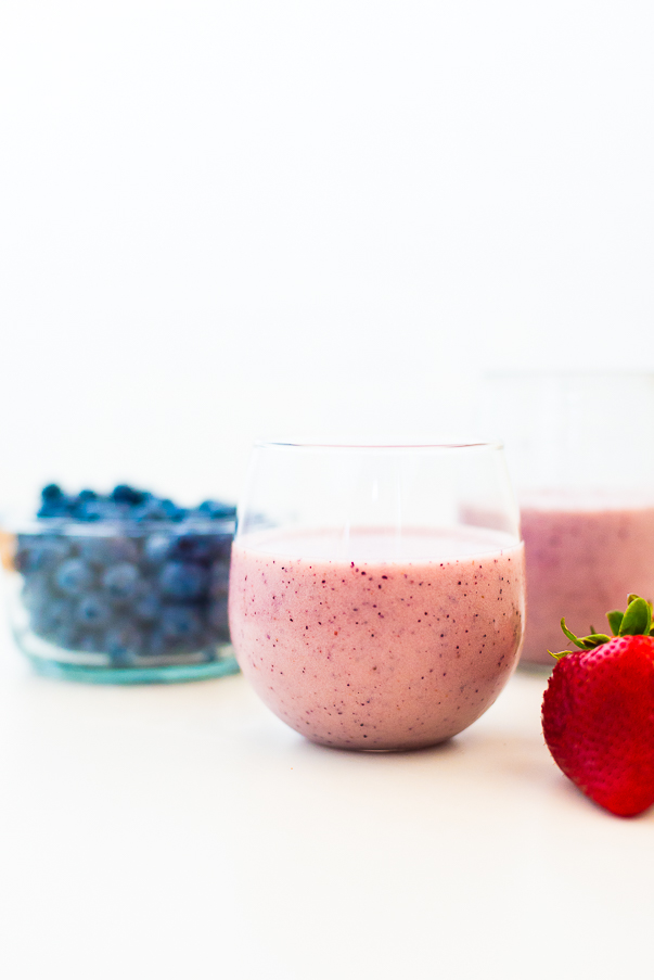 white background with two glasses filled with a strawberry blueberry smoothie and a bowl of blueberries