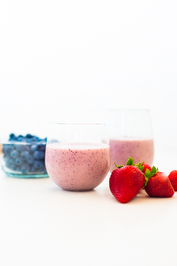 White background with two glasses of pink smoothies with strawberries and blueberries