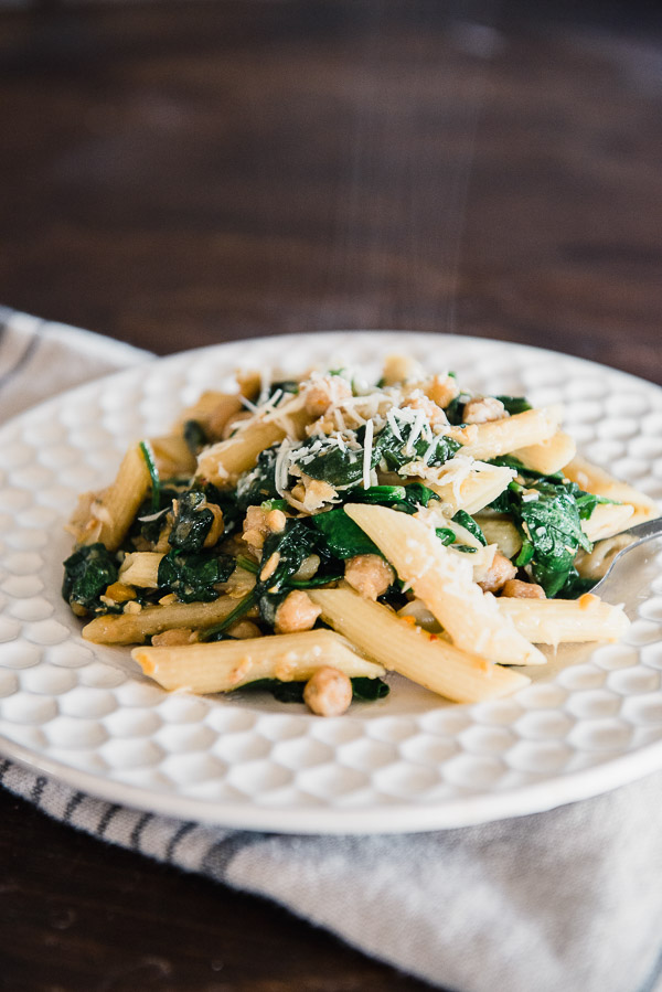 White plate with penne pasta, chickpeas, spinach and parmesan cheese