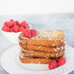 Image shows a stack of French Toast on a white plate with a blueish background