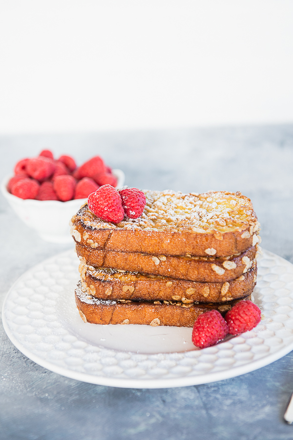 Image shows a stack of French Toast on a white plate with a blueish background